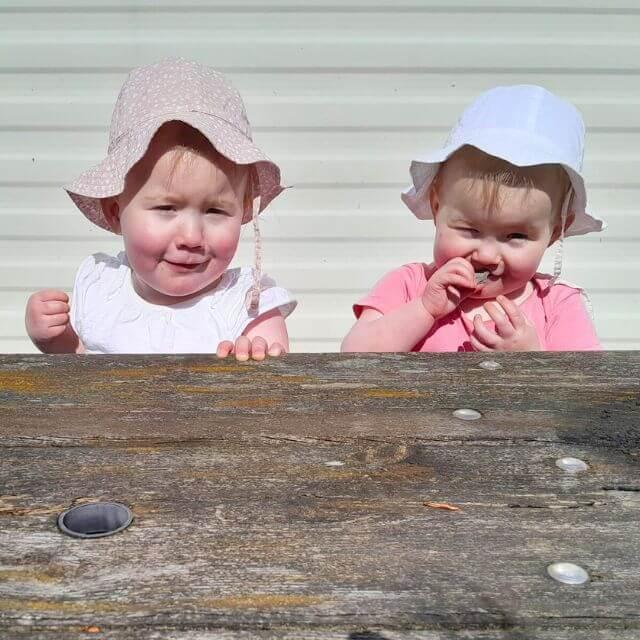 A photo taken by Katy of her twin girls sitting on the bench smiling happily.