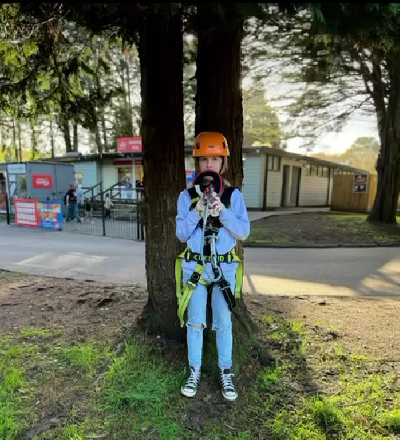 A young girl stood in front of a tree holding on to high rope equipment looking happy to be on holiday