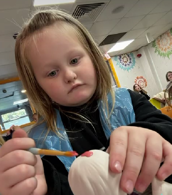 A young girl concentrating very hard, trying to paint a pot at a funny holiday activity