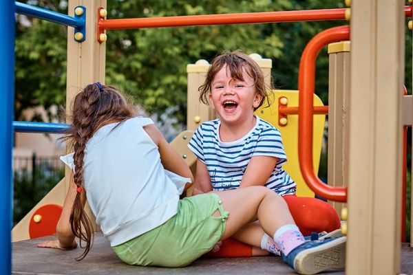 Two girls laugh as they play at a playground on holiday