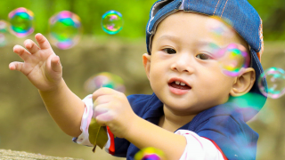 A young boy is reaching for bubbles that are floating in the air around him.