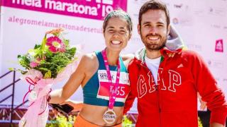 A runner is celebrating taking part in a race, and is wearing a medal and holding a bunch of flowers and hugging her partner.