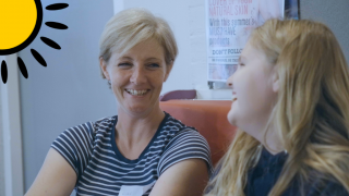 Mum Rachel, and daughter Isabelle sit on a sofa, laughing together.