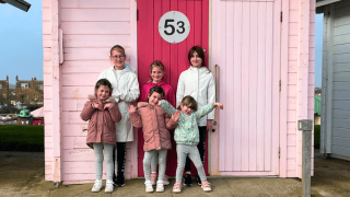 Six girls posing happily in front of a pink beach hut.