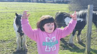 A girl posing with her hands held high in front of two ponies.