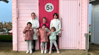 Six girls standing in front of a beach hut.