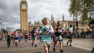 Rachel runs the London Marathon in her teal branded Family Holiday Charity t-shirt with Big Ben in the background.