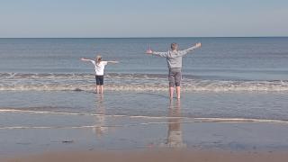 Two children raise their arms in the air while paddling in the sea on holiday