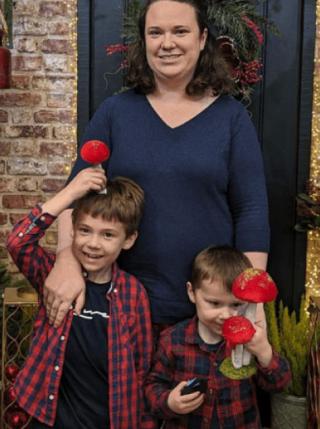 Rebecca and her two sons standing in front of a Christmas decorated house.