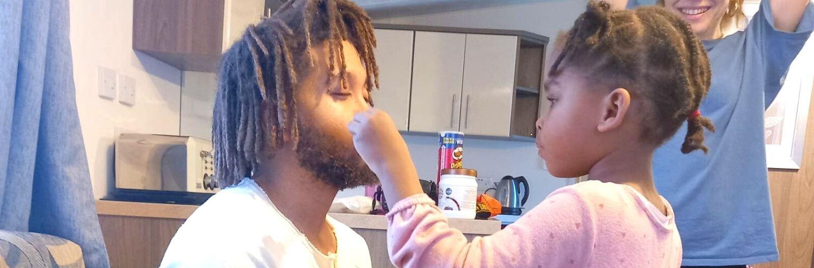 12 year old Kari feeds her uncle on her caravan holiday with Family Holiday Charity. Her aunt looks on, smiling.