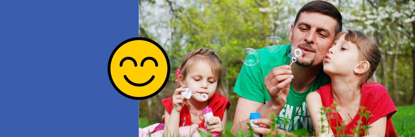 Dad and 2 daughters blow bubbles in the grass on a summer's day