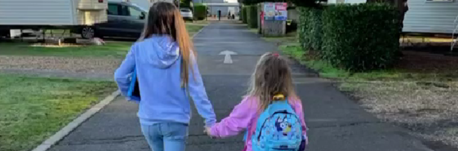 Two young girls walking holding hands while on holiday in a caravan park.