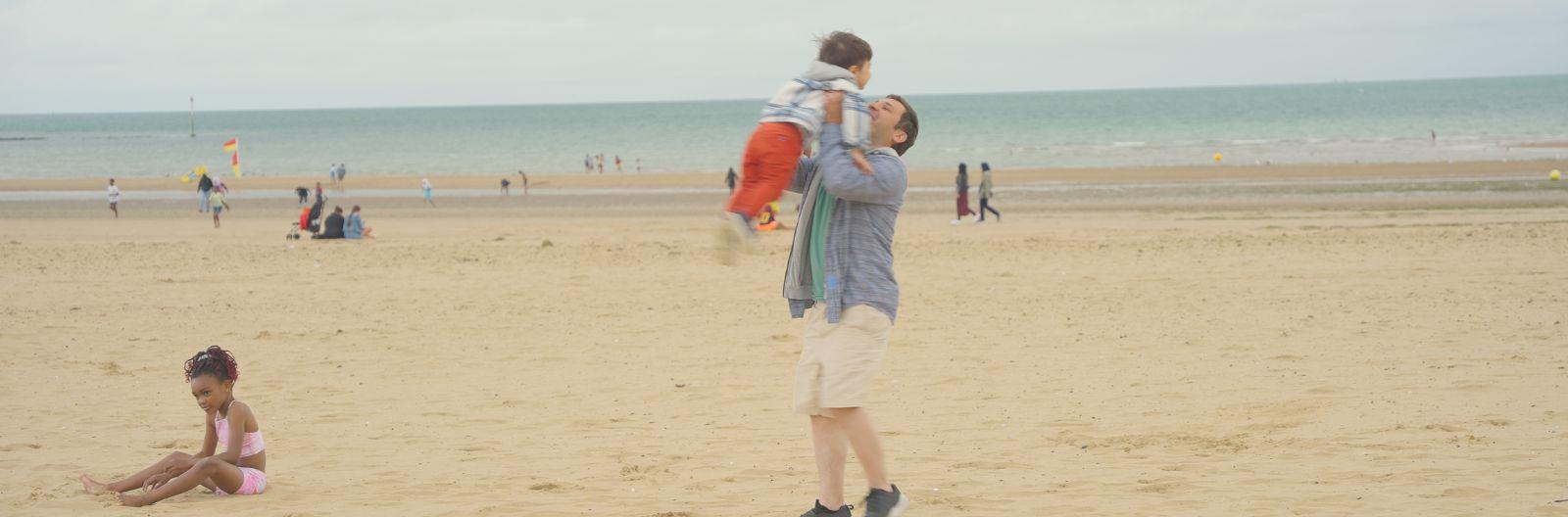 A dad holds his son in the air with a smile on the beach on holiday