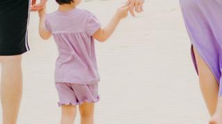 two adults and a small child walking on sand.