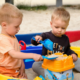 Children play in the sandpit together with brightly coloured buckets and spades on their first family holiday.
