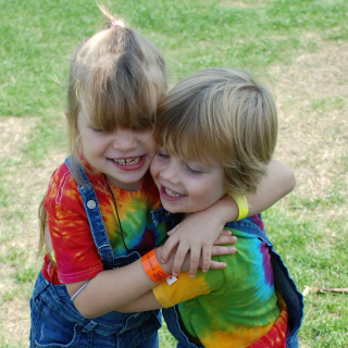 A brother and sister in matching outfits pull each other close for a hug with big smiles on their faces.