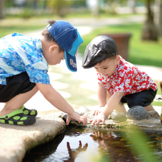 Two children play at a pool of water next to a path on a bright sunny day.