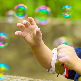 A young boy is reaching for bubbles that are floating in the air around him.