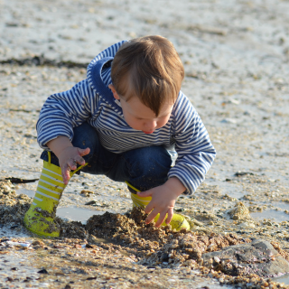A young boy bends down on the beach to play with the sand.