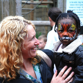 Child has their face painted to look like a lion on holiday with their carer holding them in an embrace.