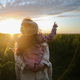 A child and parent are hugging and pointing at the sunset.