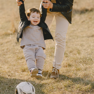 A child and their caregiver are kicking a football around a park