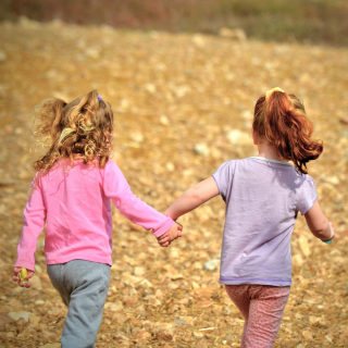 Two girls run in an autumnal field, hand in hand.