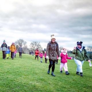 A group of families are walking together through a green field, all wrapped up in warm clothes