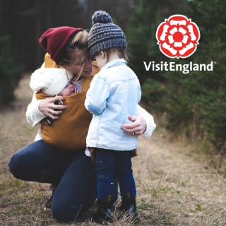 A mum hugs 2 children whilst on a walk outdoors. Visit England logo is in the top right hand corner.
