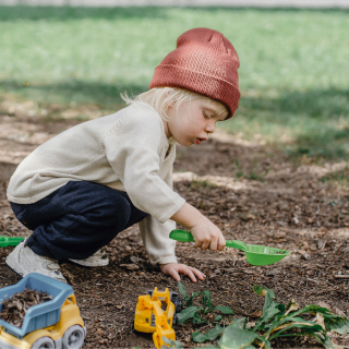 Child playing in a park with toy diggers and spades.