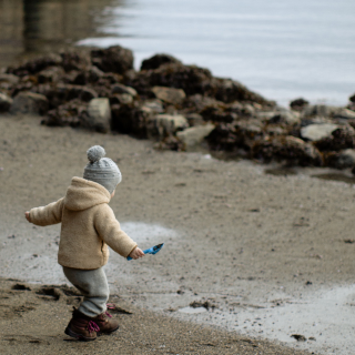 Child in winter clothing walking along the beach and looking at the sea.