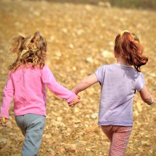 2 girls running through a dry mud field holding hands