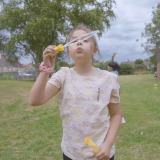 A girl is blowing bubbles in a park