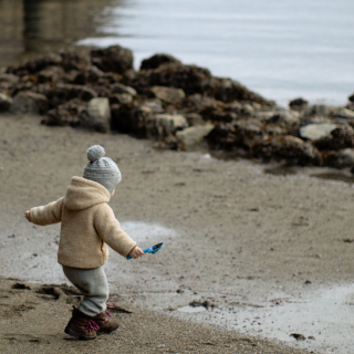 A child is playing on the beach during winter, wrapped up warm in a coat and hat.