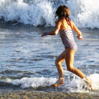 A young girl runs along the beach as the waves come rushing in.