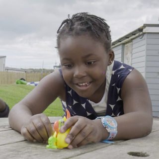A young girl is smiling whilst playing with a toy crab on her family holiday