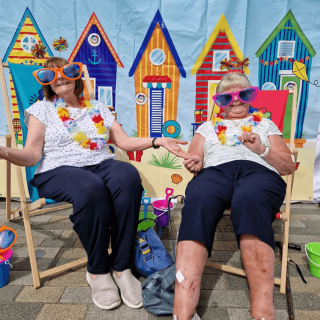 Two lovely ladies wearing goofy sunglasses sitting on beach chair.