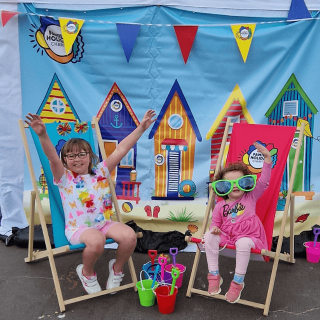 Two girls smiling happily with their hands held high sitting on beach chairs.