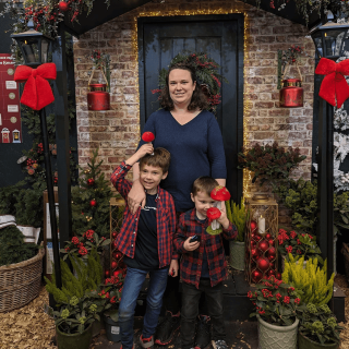 Rebecca and her two sons standing in front of a Christmas decorated house.