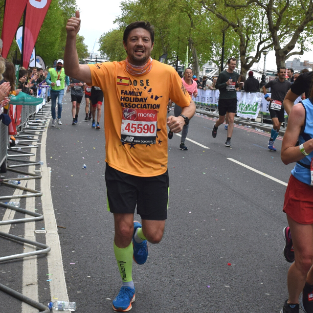 A Family Holiday Charity runner is wearing his bright yellow branded running top and a smile on his face as he waves to the team just out of shot at mile 24 of the London Marathon.