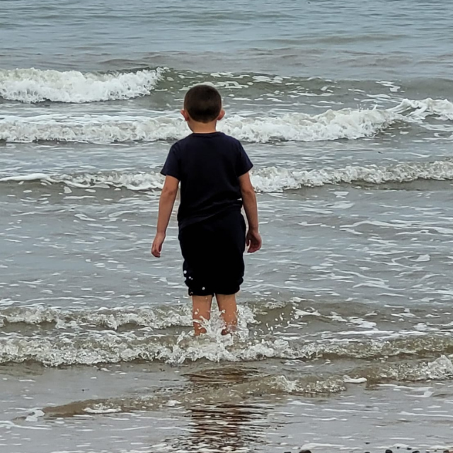 Tina's son is exploring the sea for the first time, standing with the water lapping just below his knees.