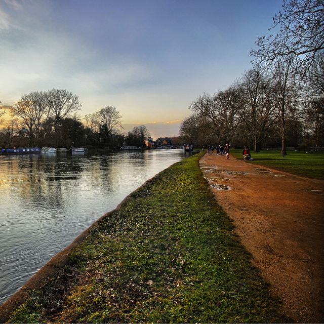 The Thames towpath running alongside the canal as the sun is setting. Walkers are making their way along the path
