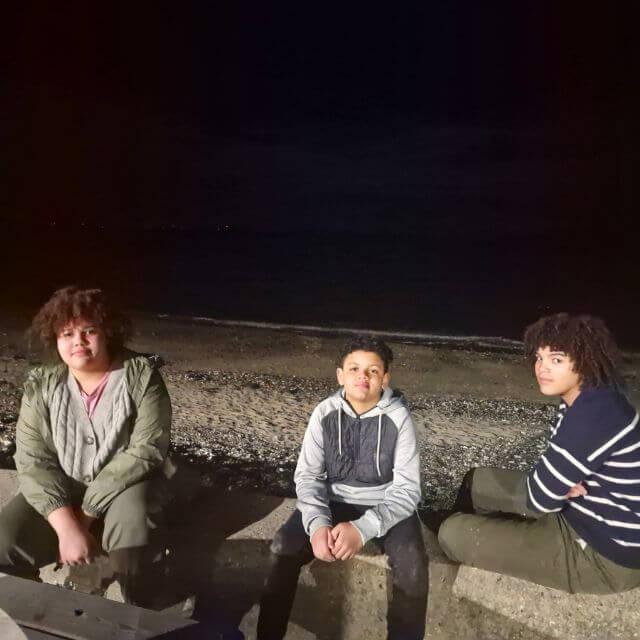 A photo taken by Stacy of her three kids sitting on the bench in a beach at night time.