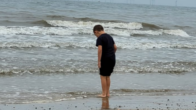 Tina's son stands at the edge of the sea, dipping his toes into the water for the first time.