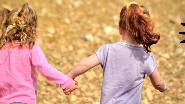 Two girls running through a dry mud field holding hands