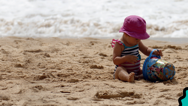 A child plays with a bucket and spade on the beach on a family holiday