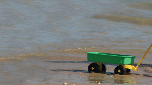 A child pulls a toy trolley along the beach on holiday