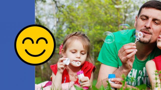 Dad and 2 daughters blow bubbles in the grass on a summer's day
