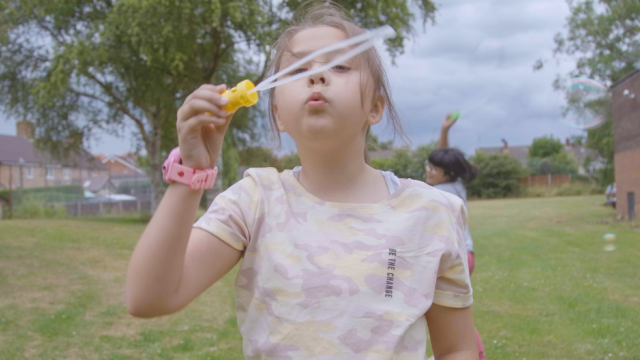 A child blows bubbles in a green park.