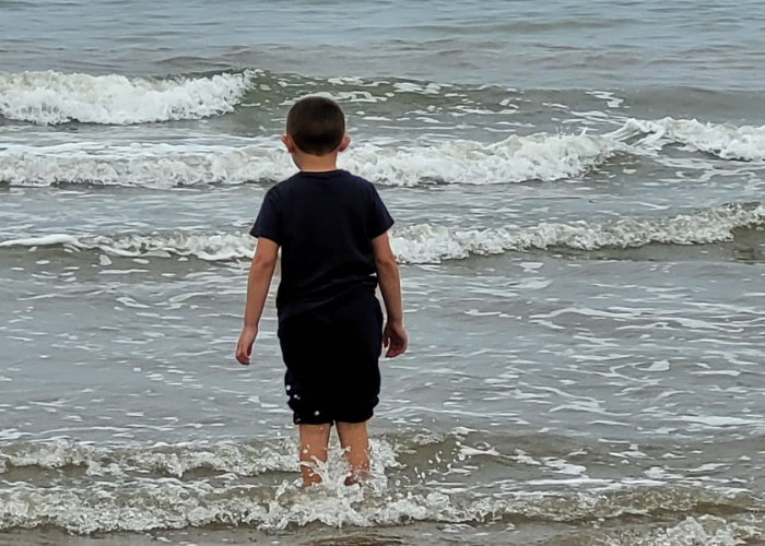 Tina's son is exploring the sea for the first time, standing with the water lapping just below his knees.